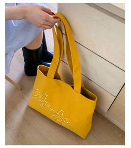Close-up of bright yellow canvas tote bag with white pearl star detail on surface