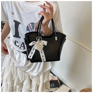 Detail of black glossy bucket bag with lace bow and pearl heart pendant charm