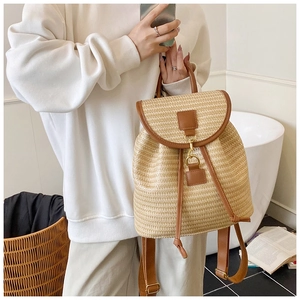 Dettaglio dello zaino in paglia intrecciata con spalline in pelle marrone tenuto da una modella