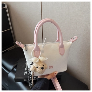 Détail d'un sac seau en cuir blanc avec poignées roses et breloque chien en peluche