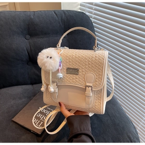 Vue détaillée d'un sac bandoulière crème tressé avec pendentif en peluche et boucles