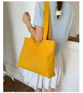 Detailed shot of yellow canvas tote bag with star rivets on shoulder during use