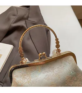 Close-up of golden carved metal handle with pearl accents on a Chinese embroidery bag