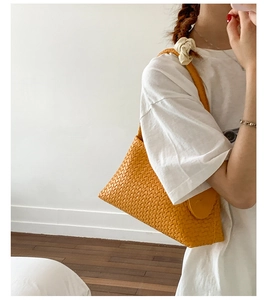 Detail of woven texture and round handle on orange leather underarm hobo bag