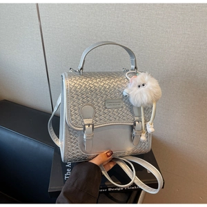 Détail du sac à dos argenté avec texture tressée, boucles en métal et charm monstre en peluche