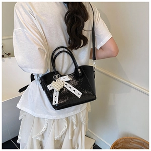 Detail of a black patent leather handbag with lace bow and pearl heart charm on a model