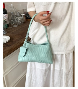 Close-up of light green woven leather hobo bag with a side round pendant charm
