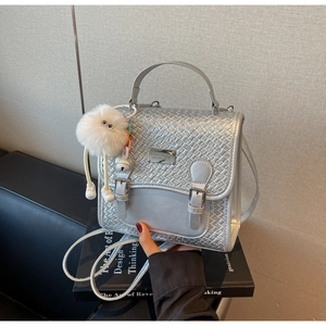 Détail d'un sac argenté en PU tressé avec boucle en métal et porte-clés peluche