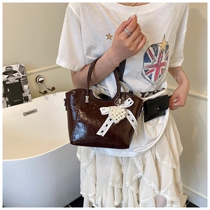 Detail of dark brown patent leather bucket bag with lace bow and pearl heart charm