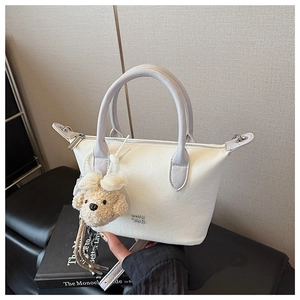 Détail du sac à main crème élégant avec poignée mauve, logo de marque et ours en peluche