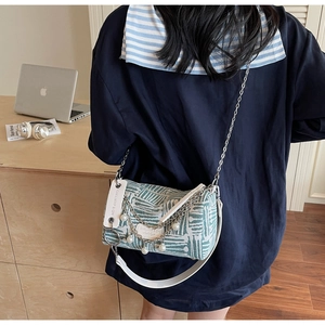 Detail of green woven cylinder bag with metal chain, pearl charm and leather strap