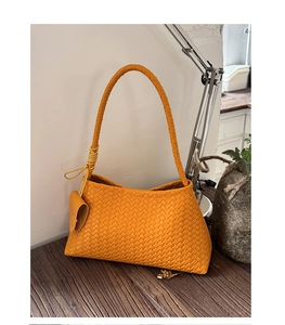 Detailed view of yellow woven leather underarm bag with a small heart-shaped pendant detail