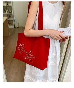 Detail of red canvas tote bag featuring silver studded star accents and wide shoulder strap