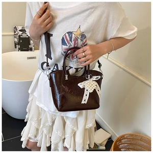 Detail of vintage brown patent leather bucket bag with white lace bow and pearl heart charm