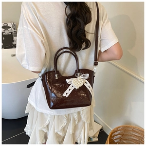 Detail of dark brown patent leather bucket bag with lace bow and pearl heart pendant