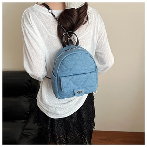 Close-up of blue denim quilted backpack with chain strap on a person's shoulder