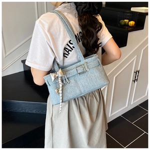 Close-up of light blue denim shoulder bag with silver bow charm and heart pendant detail