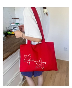 Red canvas tote bag detail featuring metallic star studs and spacious shoulder design