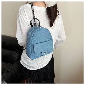Close-up of quilted denim backpack featuring chain straps and silver twist lock detail