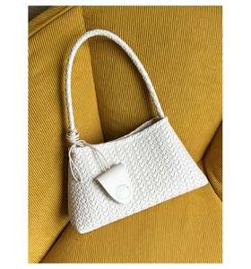Detailed view of white woven shoulder bag with side tassels on a texture sofa