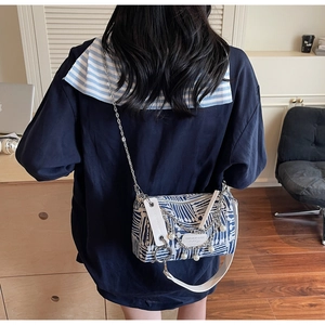 Detail of canvas crossbody bag with silver chains and pearl charms on blue-white texture