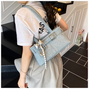 Detail of light blue denim tote bag with golden buckle and bow charm on shoulder