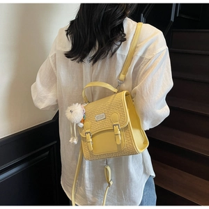 Détail du sac bandoulière jaune tressé avec pompon blanc porté par un mannequin