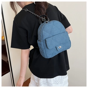 Close-up of blue quilted denim mini backpack with metal chain straps and twist-lock detail