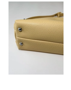 Detailed close-up of light yellow pebbled leather handbag base with silver protective metal studs