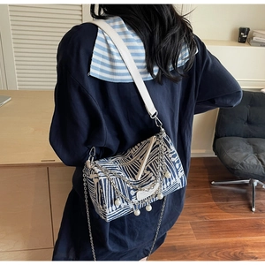 Detail of canvas pillow bag with blue abstract pattern, metal chains, and pearl charms