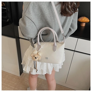 Vue détaillée d'un sac seau crème avec poignée violette et charm d'ours en peluche