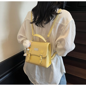 Détail du sac à dos jaune matelassé avec pompon blanc et lanières à boucles en métal