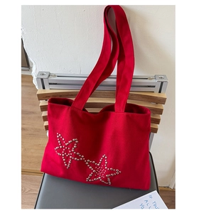 Detail of red canvas tote bag featuring decorative silver metal star-shaped rivets on surface