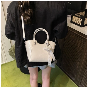 Detail of cream bucket bag featuring wave-shaped rim and pearl heart charm accessory