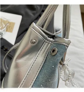 Detail view of silver metallic leather and blue denim patchwork handbag with pearl charm