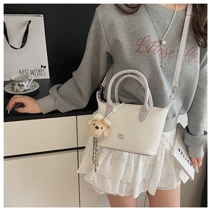 Détail du mini sac seau blanc avec anse violette et breloque ours en peluche sur modèle