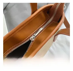 Detailed close-up of smooth silver metal zipper and brown leather trim on canvas handbag