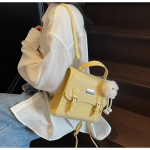 Détail du sac à dos jaune avec rabat en texture tissée et pendentif boule peluche