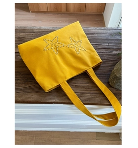Detailed top view of a yellow canvas tote bag with metal rivet star patterns on a table