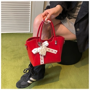 Detail of red leather bucket bag with pearl heart pendant and bow charm accessory
