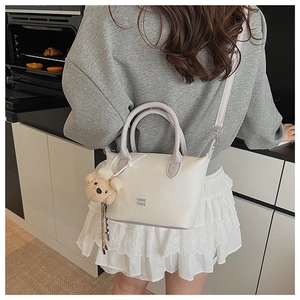 Vue détaillée du sac seau blanc cassé avec pendentif ours et texture en simili cuir