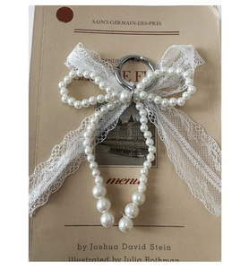 Detailed macro view of vintage pearl and lace bow charm with silver clasp on a book