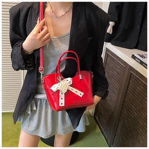 Detail of red patent leather bucket bag with white pearl bow and adjustable strap