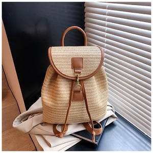 Detail of woven straw backpack featuring brown leather trim and golden metal clasp