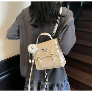 Détail du sac à dos crème avec texture tressée, doubles boucles et pendentif en peluche