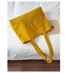Detail of mustard yellow canvas tote bag featuring decorative twin pearl star patterns