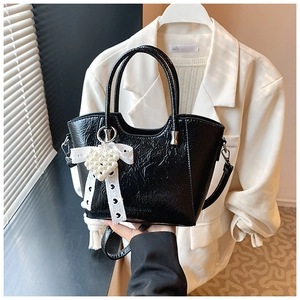 Detail of black patent leather bucket bag with white lace bow and heart pearl charm