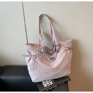 Detail of light purple nylon tote bag with side drawstrings and fashion label on leather sofa