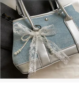 Detail of light blue denim handbag featuring silver handles and white lace bows with pearls