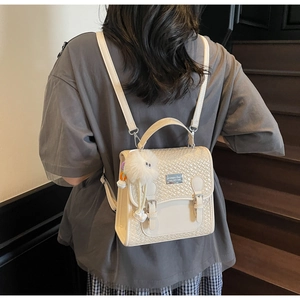 Détail d'un sac à dos beige avec rabat tissé, boucles argentées et un porte-clé peluche